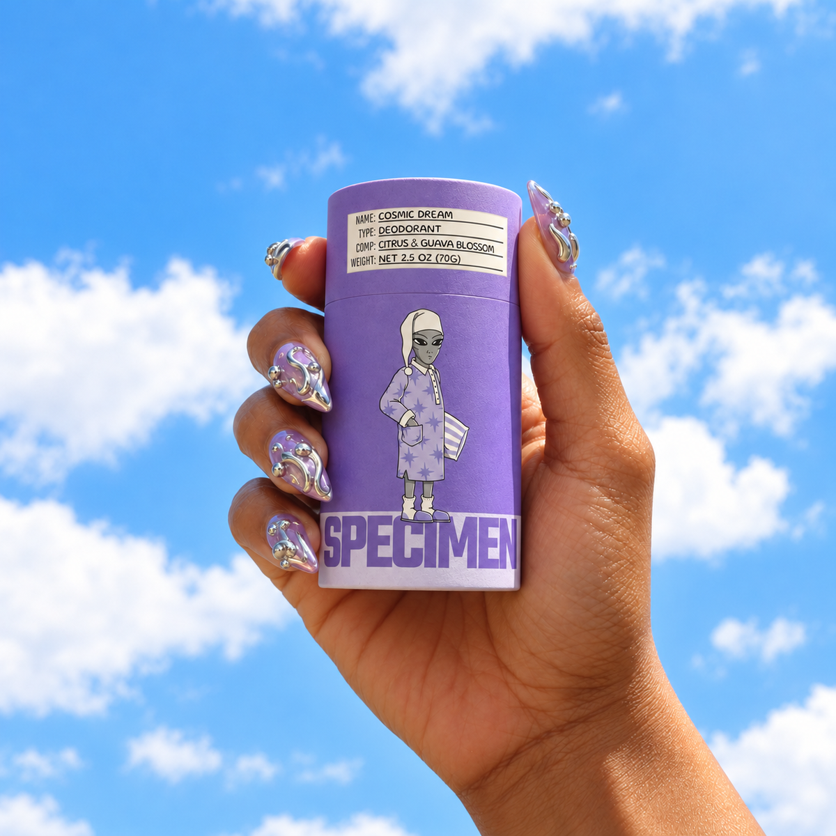 Hand with chrome nails holding Specimen Cosmic Dream aluminum-free deodorant against a bright blue sky