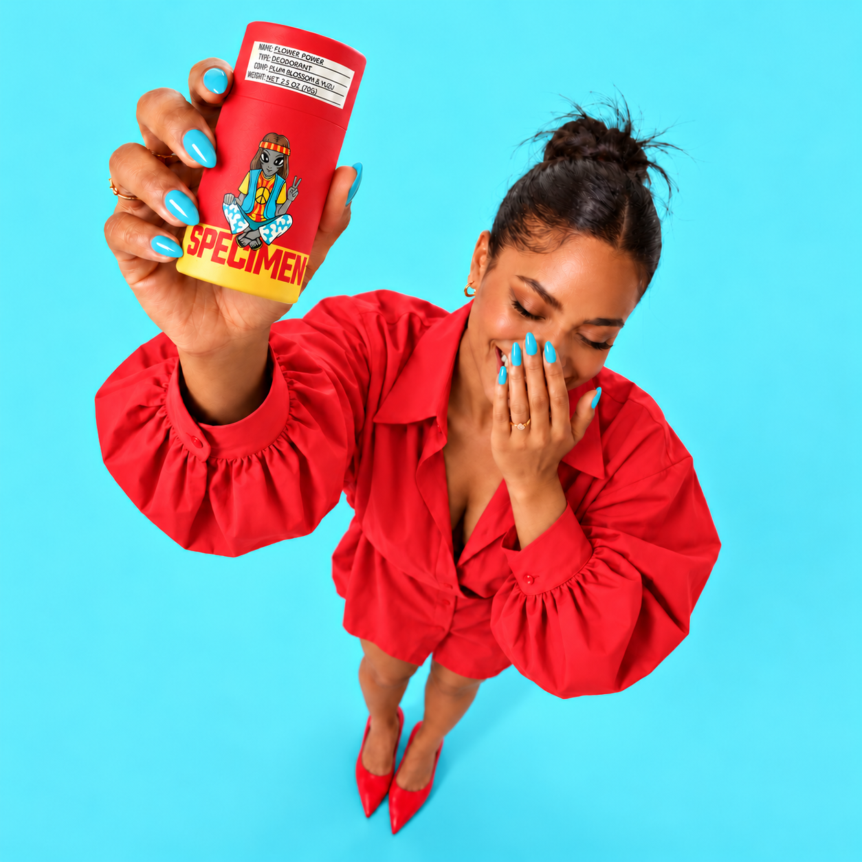 Woman in a red dress laughing and holding up Specimen Flower Power aluminum-free deodorant on a turquoise background