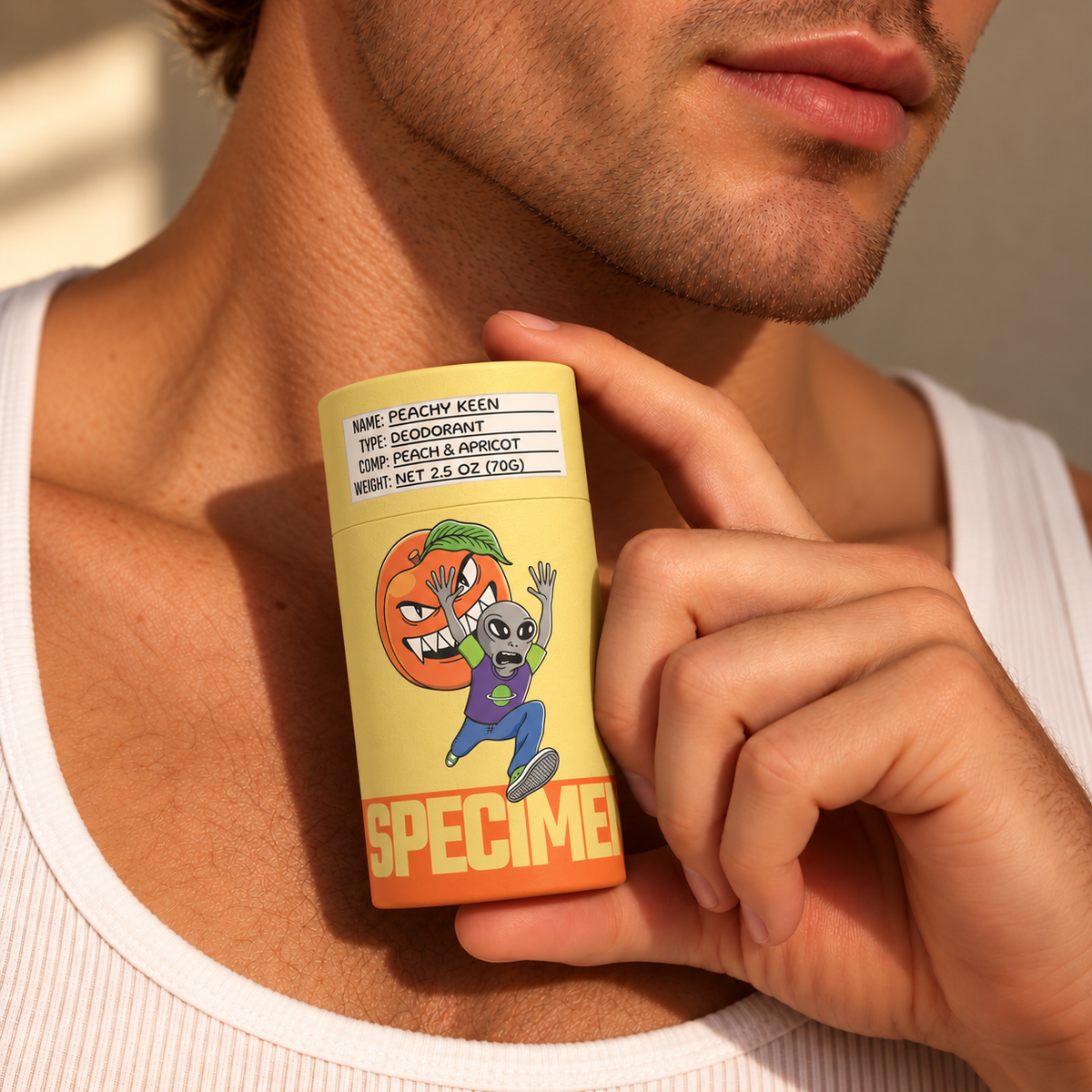 Man in a white tank top holding Specimen Peachy Keen aluminum-free deodorant in plastic-free packaging