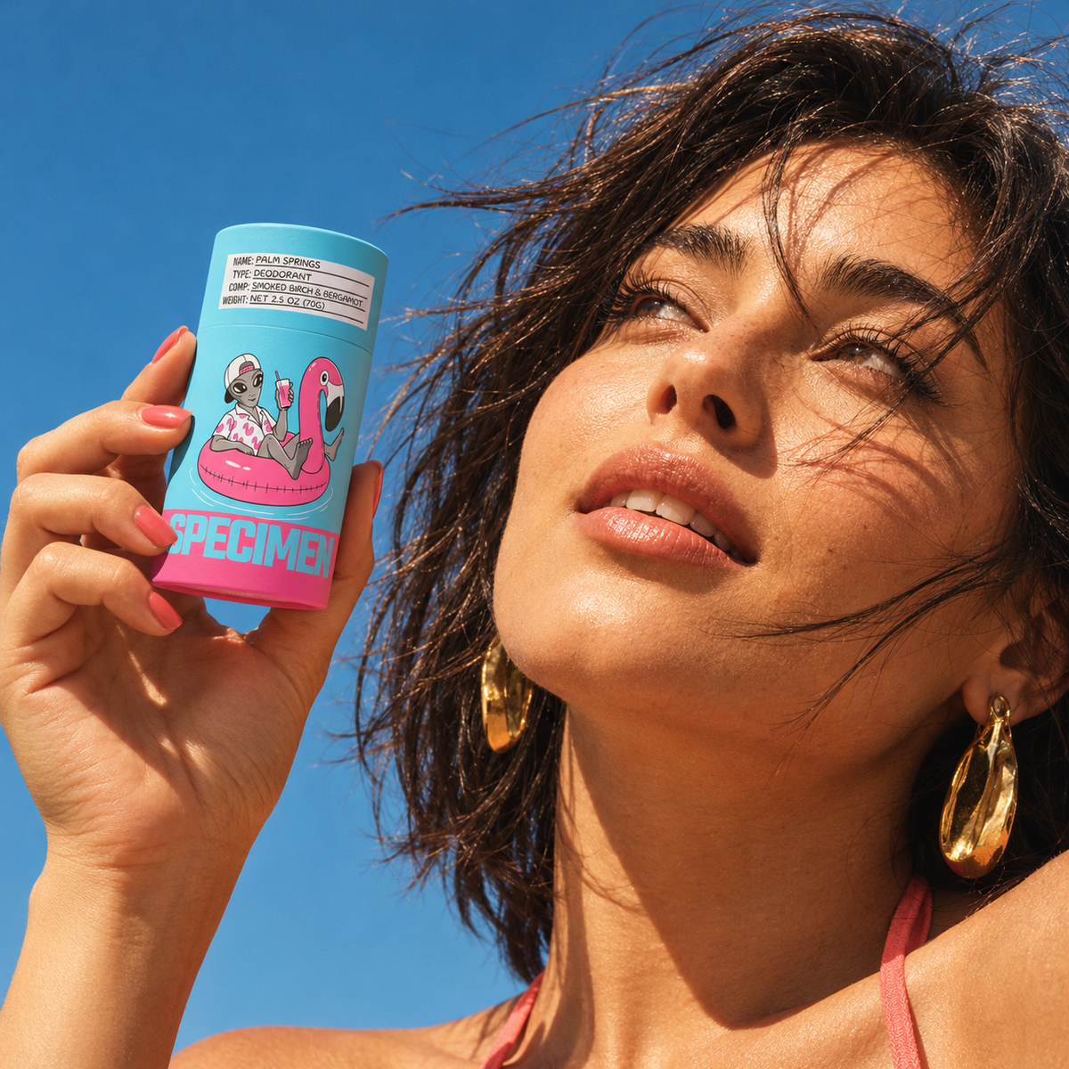 Woman in gold hoop earrings holding Specimen Palm Springs natural deodorant up to the sun