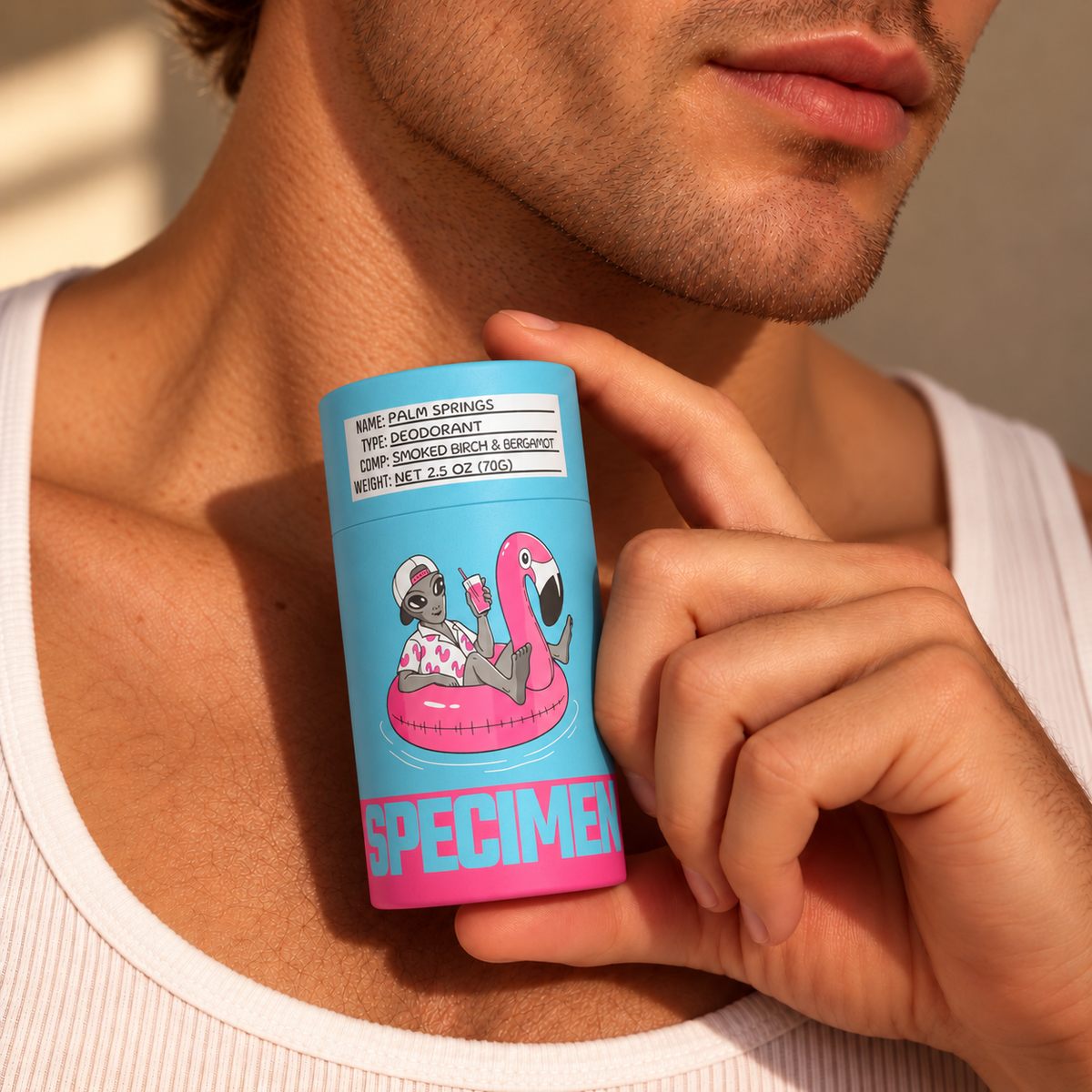 Man in a white tank top holding Specimen Palm Springs bergamot and smoked birch deodorant in plastic-free packaging